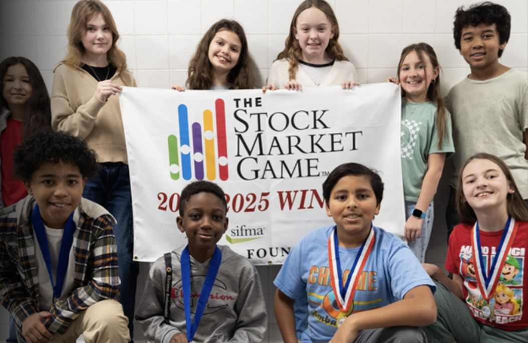 Students wearing medals hold a Stock Market Game 2024–2025 Winner banner