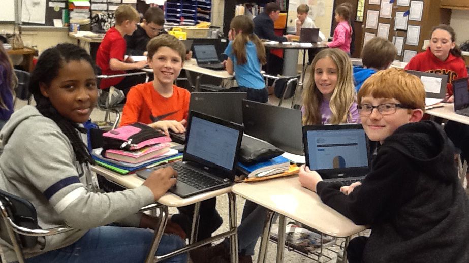 Students smiling while working on laptops in class
