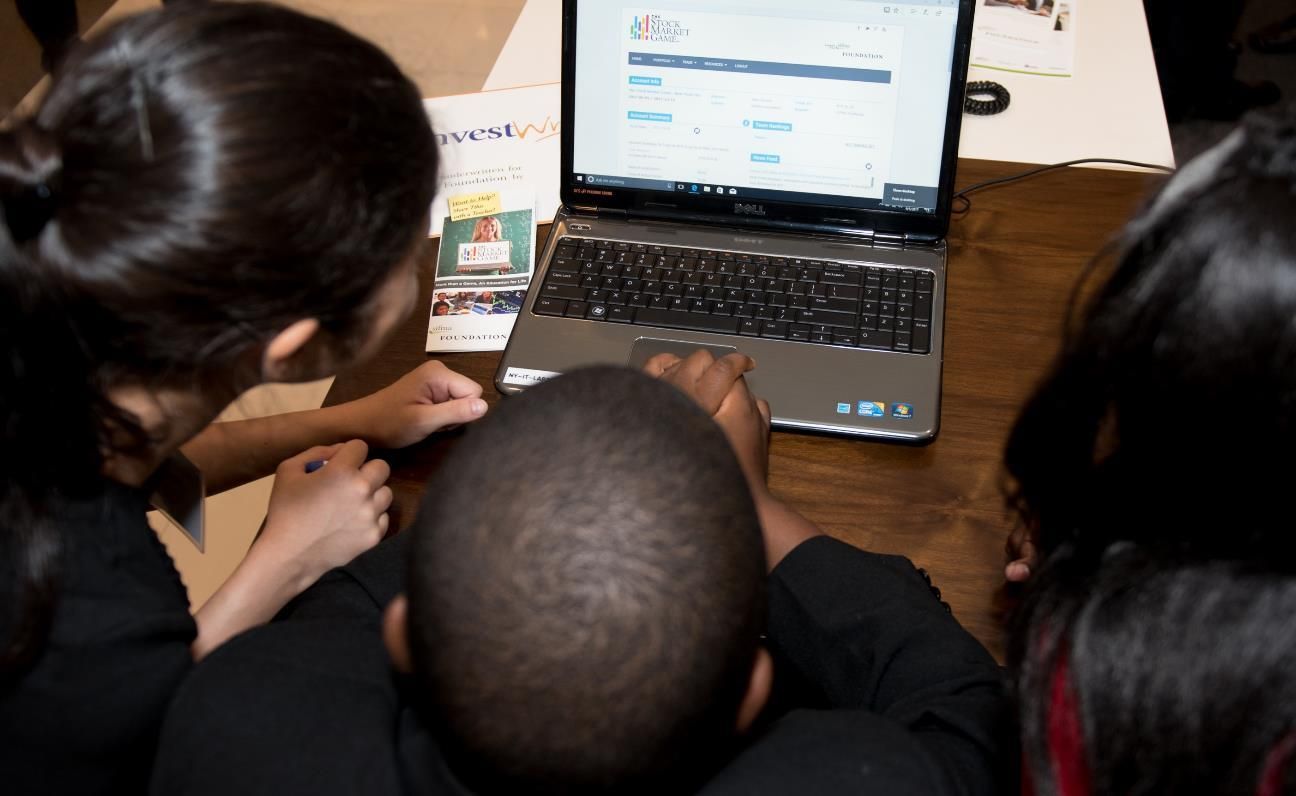 Students looking at a Stock Market Game screen on a laptop