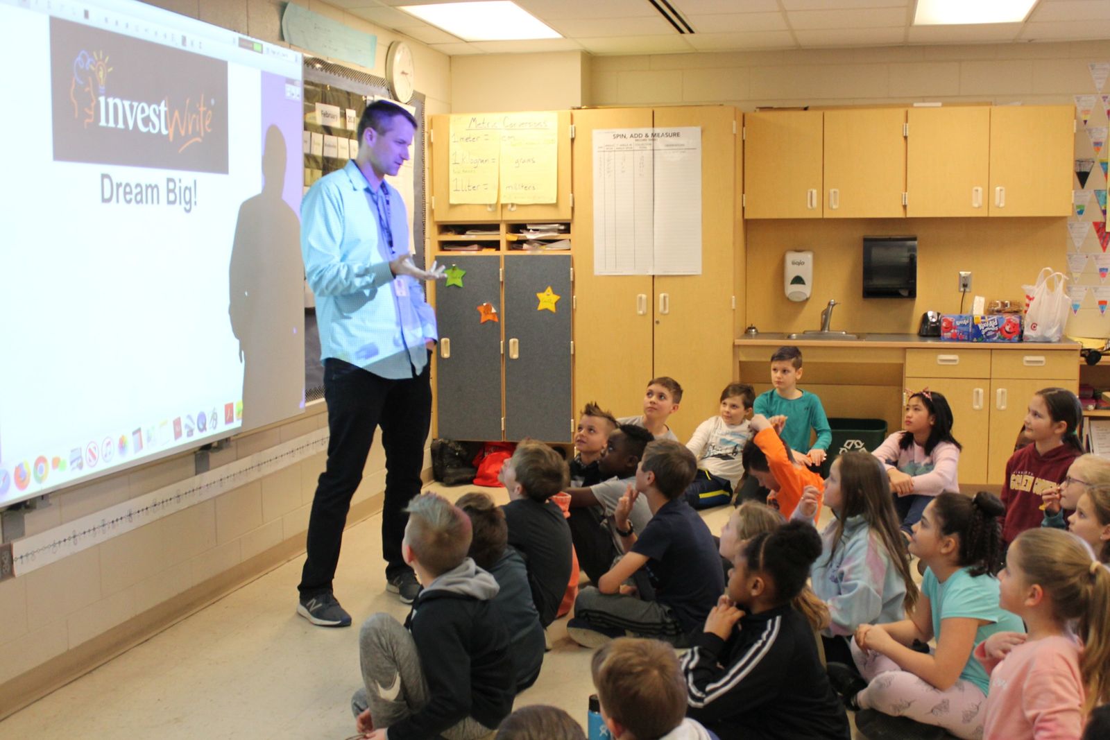 A presenter in front of an InvestWrite slide with students seated on the floor