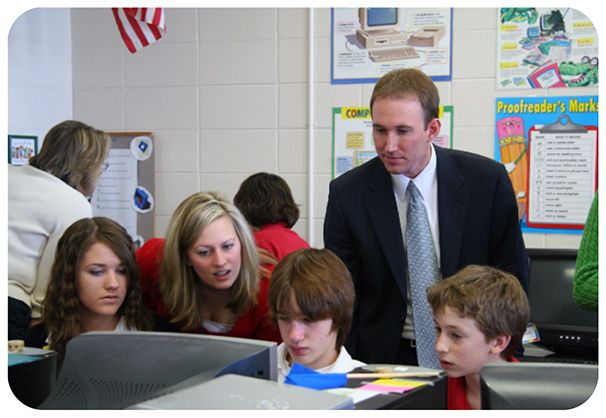 A financial professional working with students at a classroom computer